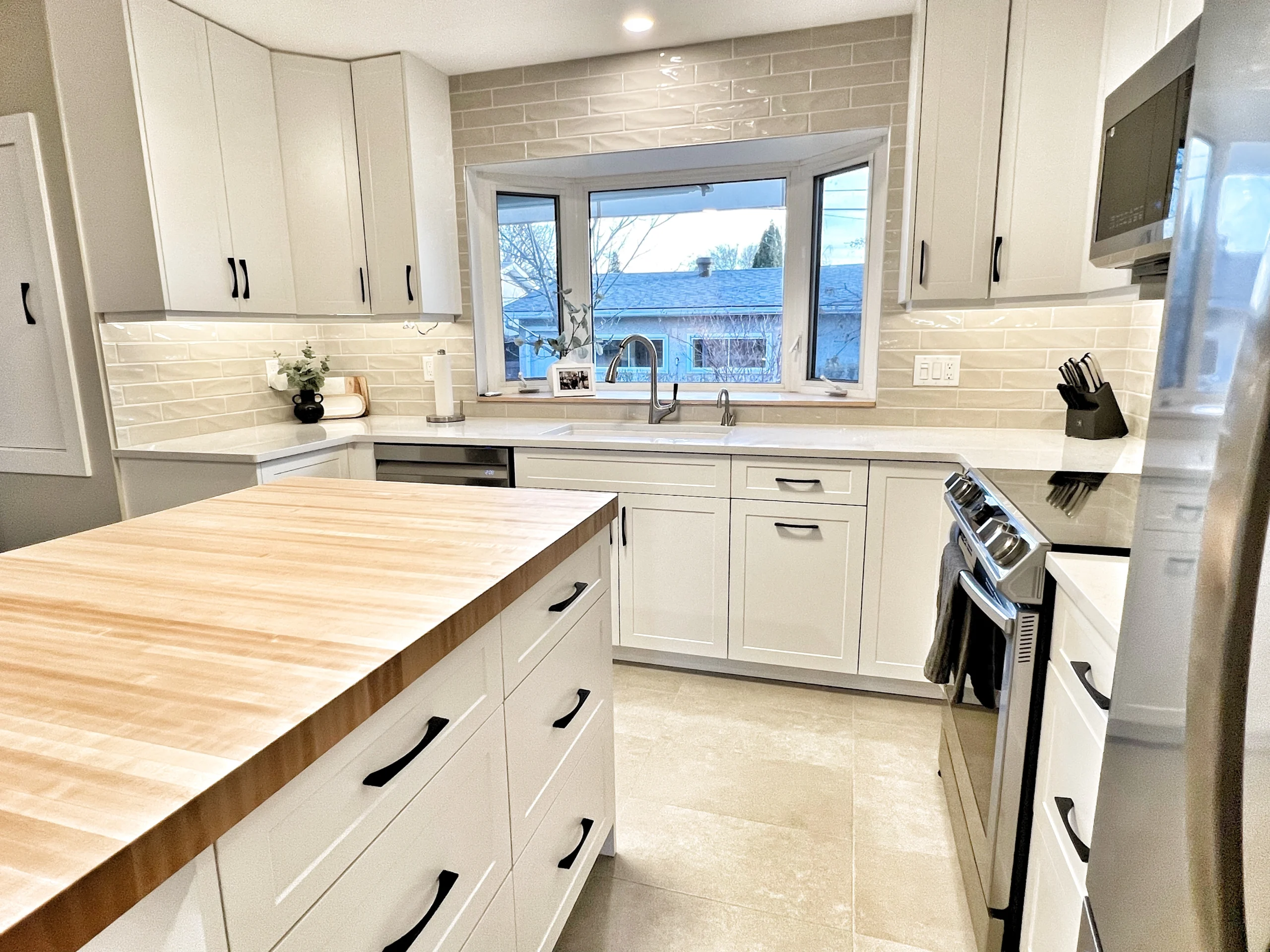 Mid-range Calgary kitchen renovation with white cabinets, butcher block island, subway tile backsplash, and functional layout